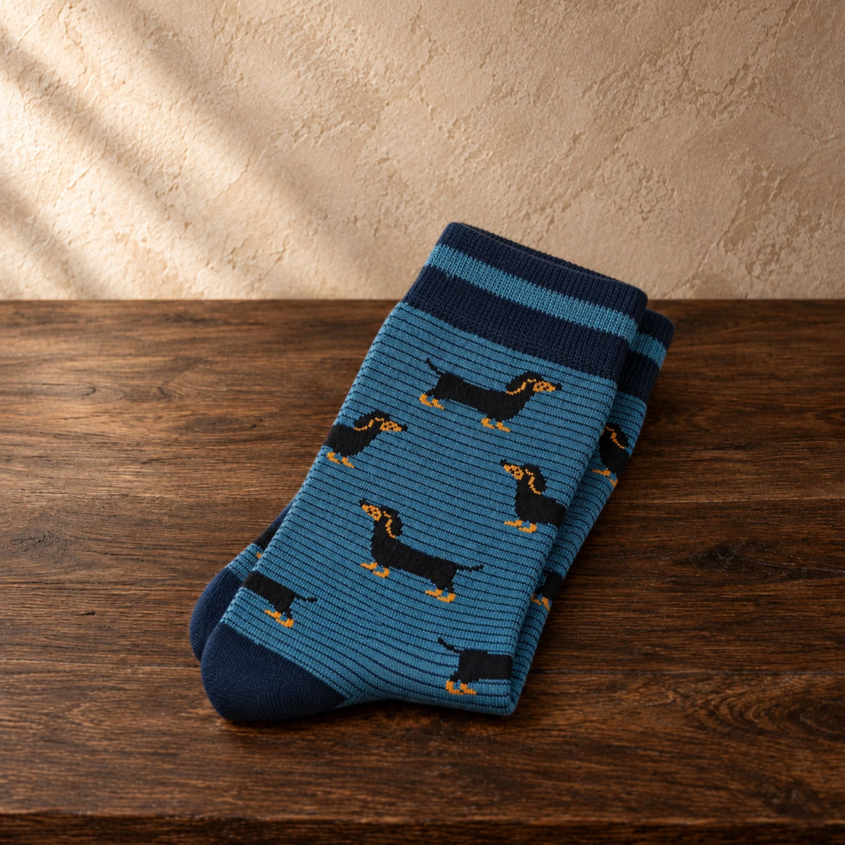 A pair of blue striped socks with a dachshund dog pattern, folded on a dark wooden surface against a textured beige wall.