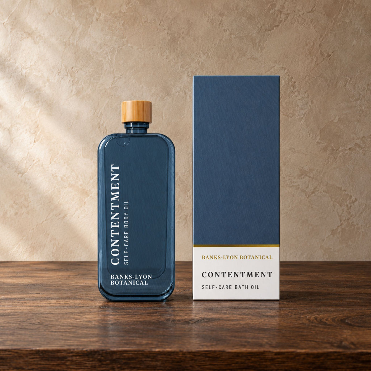 A dark blue bottle of Banks-Lyon Botanical Contentment Self-Care Bath Oil stands next to its matching dark blue box on a wooden surface against a textured beige wall.