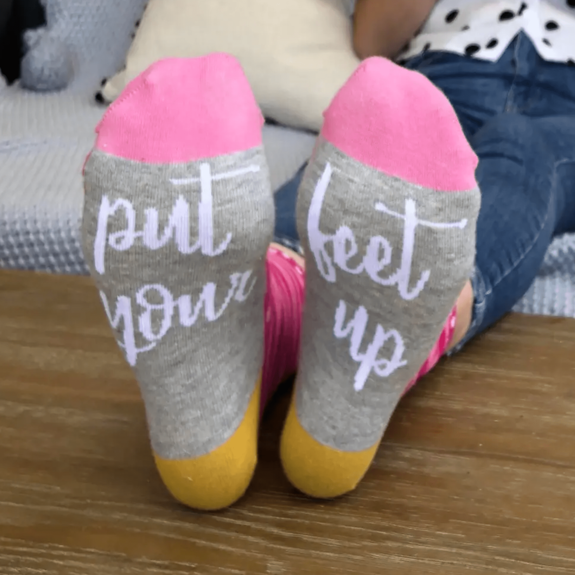 Grey socks with pink toes and yellow heels, worn by a person sitting on a sofa with their feet up.