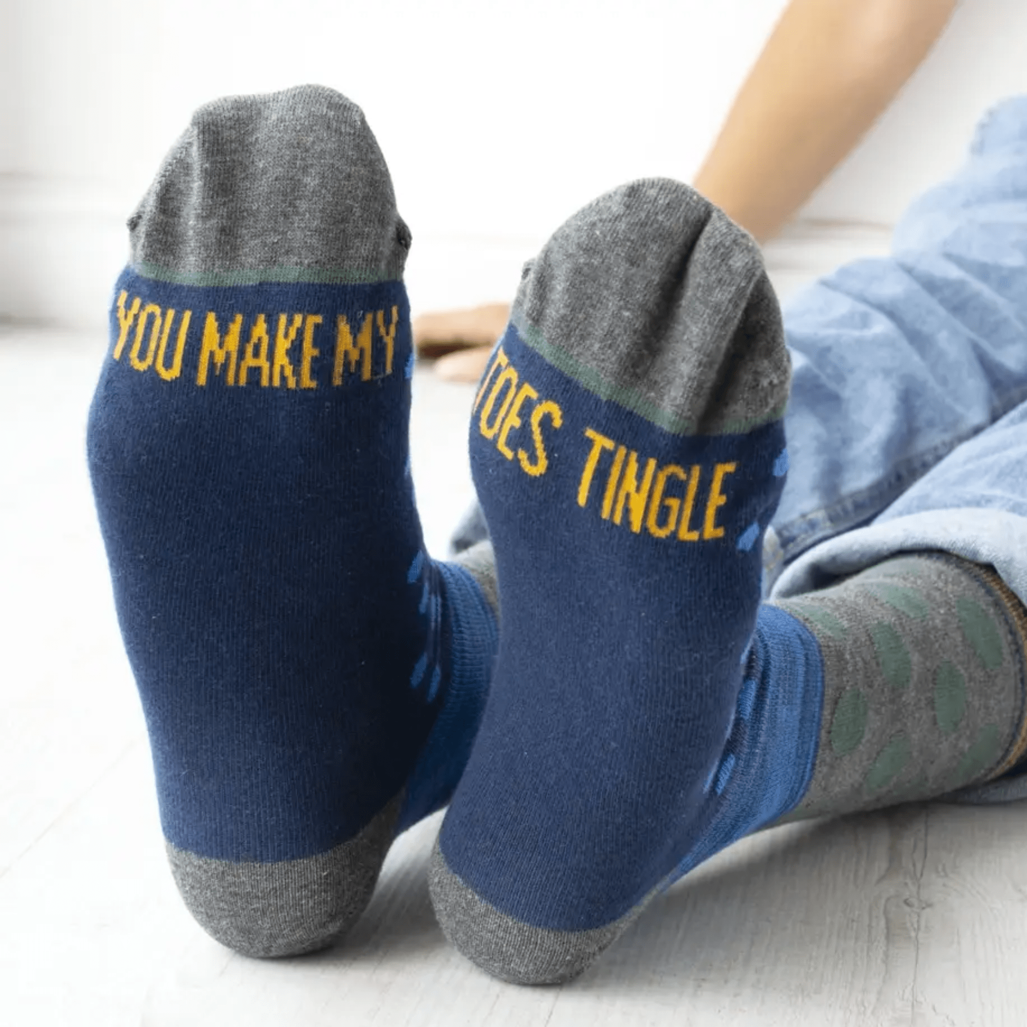 Blue socks with yellow 'you male my toes tingle' text worn by a person sitting on the floor.