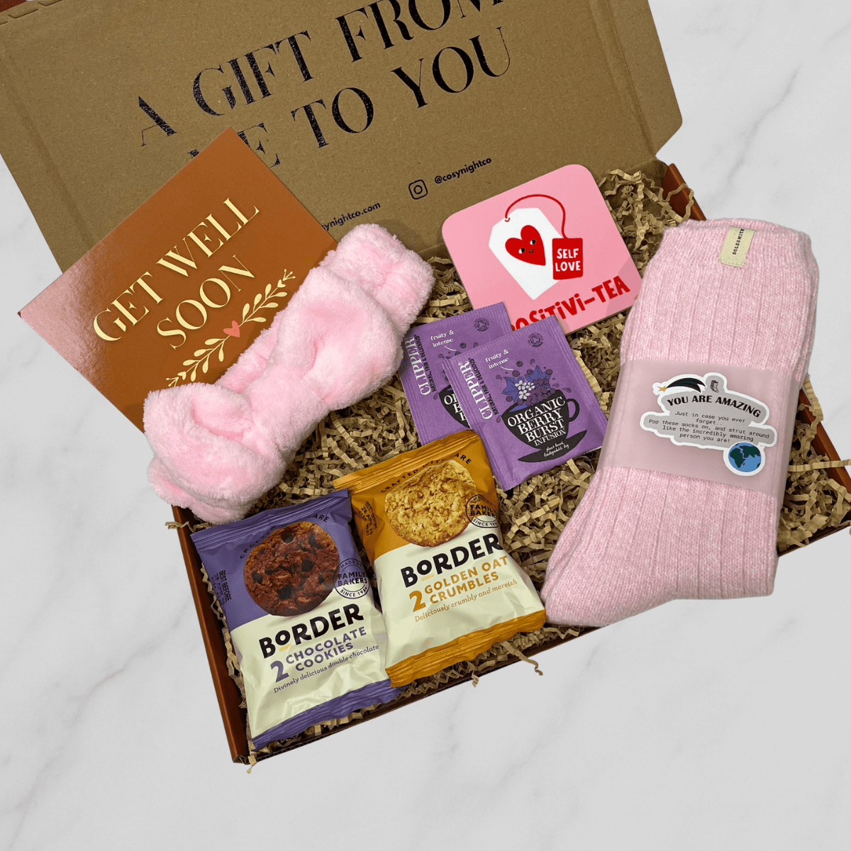 Get well soon letterbox gift box with cosy pink socks, biscuits, tea, pink headband and coaster.