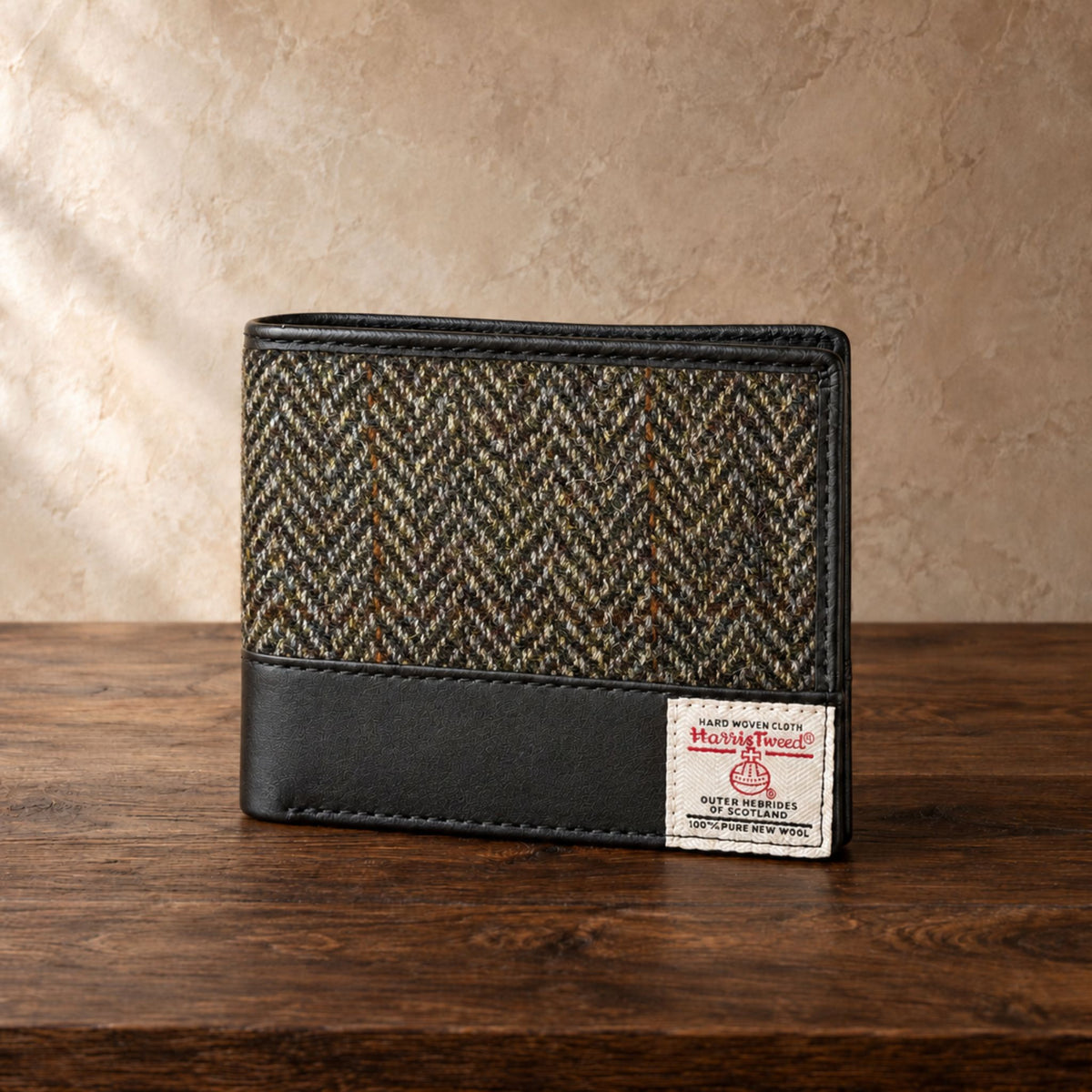 Green and brown tweed wallet with a leather lining and a Harris Tweed tag on a dark oak table against a beige textured wall.