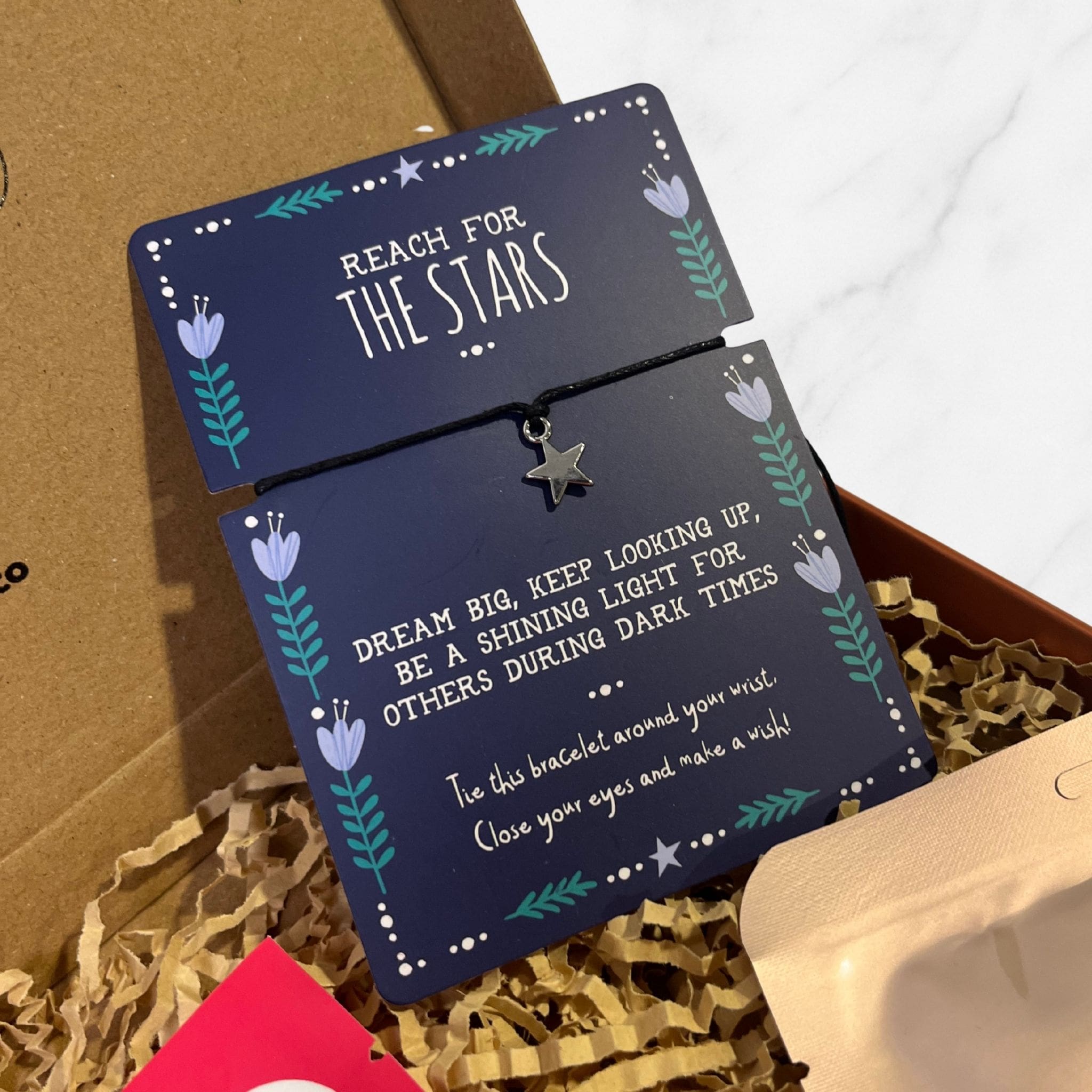 “Reach for the Stars” bracelet with a small star charm on a navy backing card featuring an inspirational message