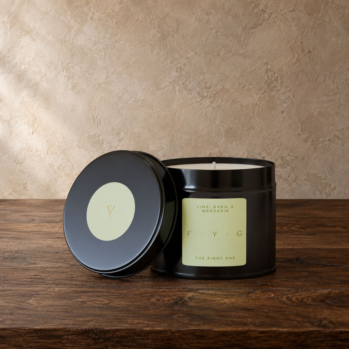 A black metal candle tin with its lid leaning beside it on a wooden surface. The candle label is pale green.