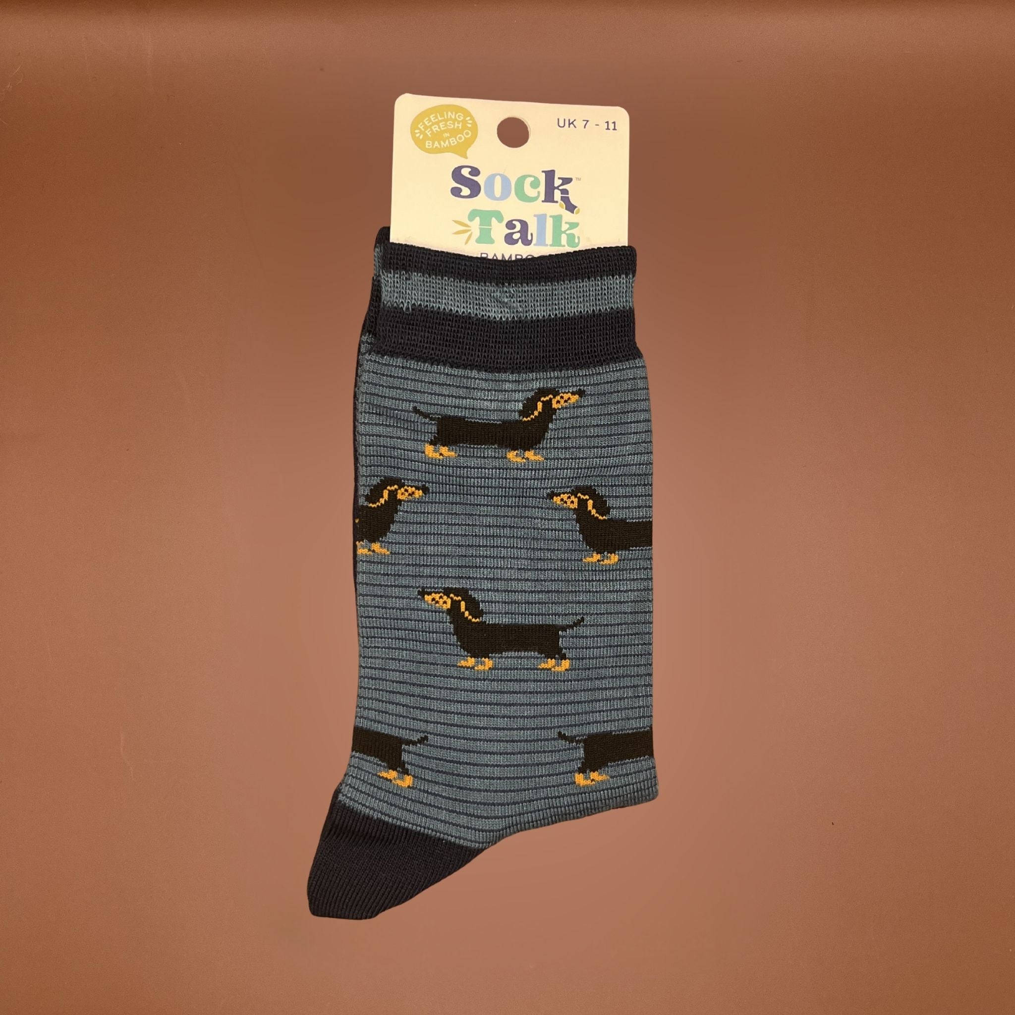 Pair of blue bamboo socks with navy cuffs and heels, featuring a repeating pattern of small black and tan dachshunds.