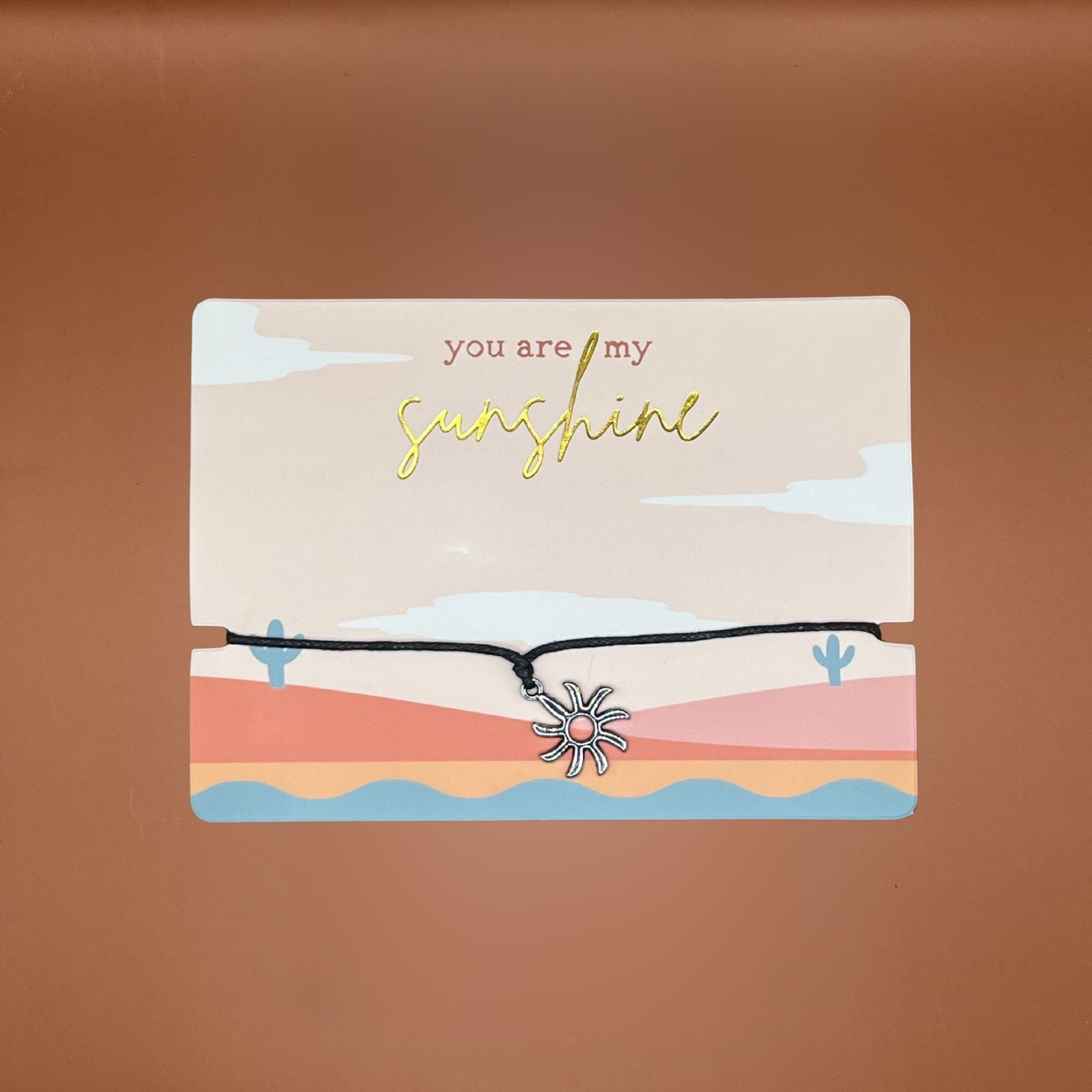 Card with 'you are my sunshine' text and a sun-shaped pendant on a desert landscape illustration.