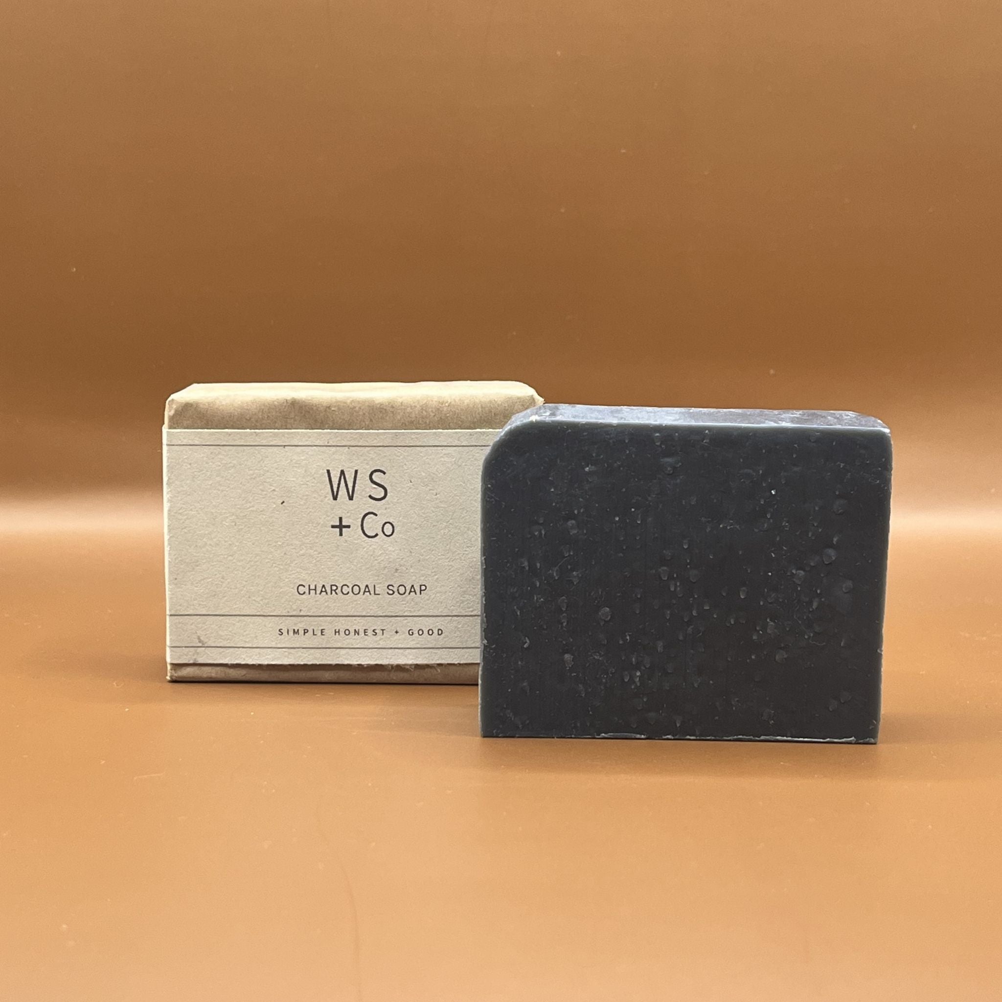 Bar of charcoal soap next to packaged soap labeled charcoal soap in brown paper packaging