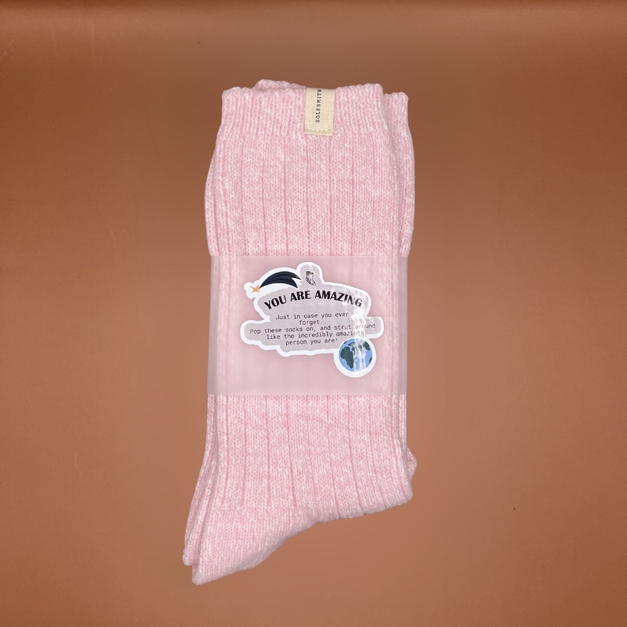 Pink socks with a 'You are amazing' label on a brown background