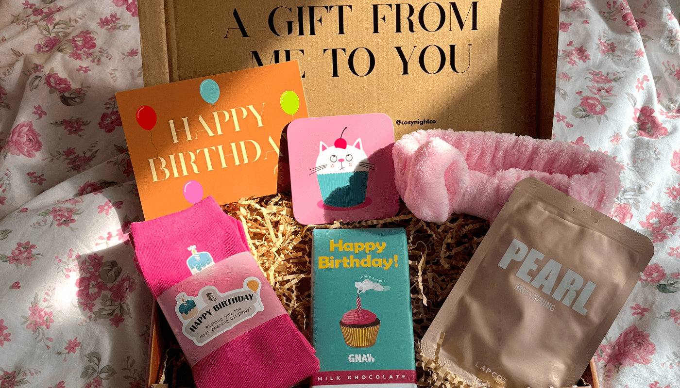 Gift set with 'Happy Birthday' cards, socks, and a chocolate bar on floral bedding.