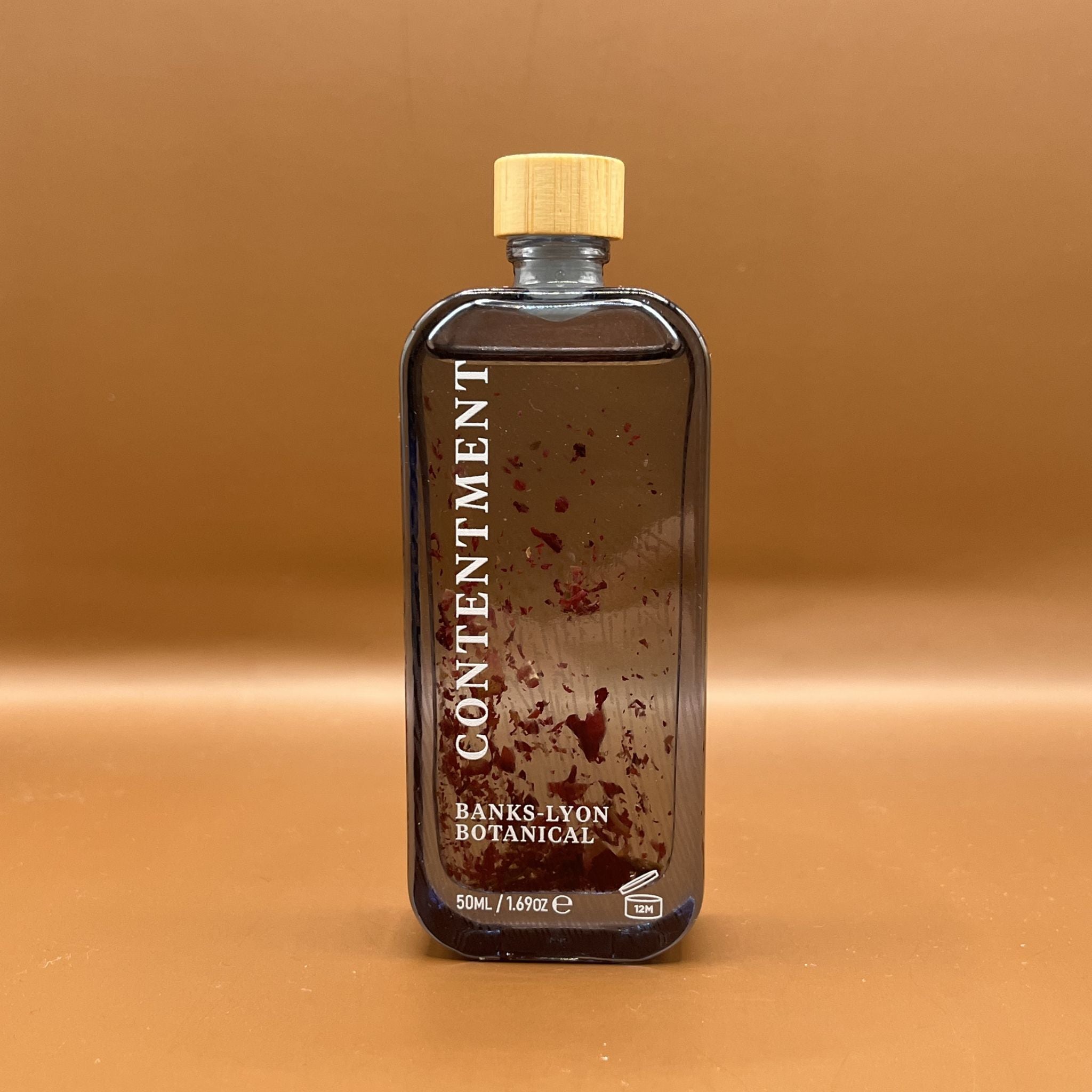 Bottle of Contentment Banks Lyon Botanical bath oil with rose petal pieces inside the blue glass bottle