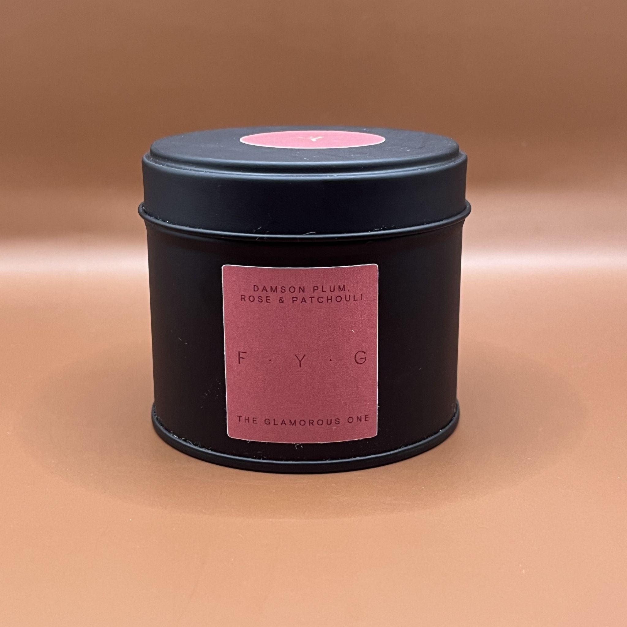 Black candle tin with pink label saying damson plum rose and patchouli