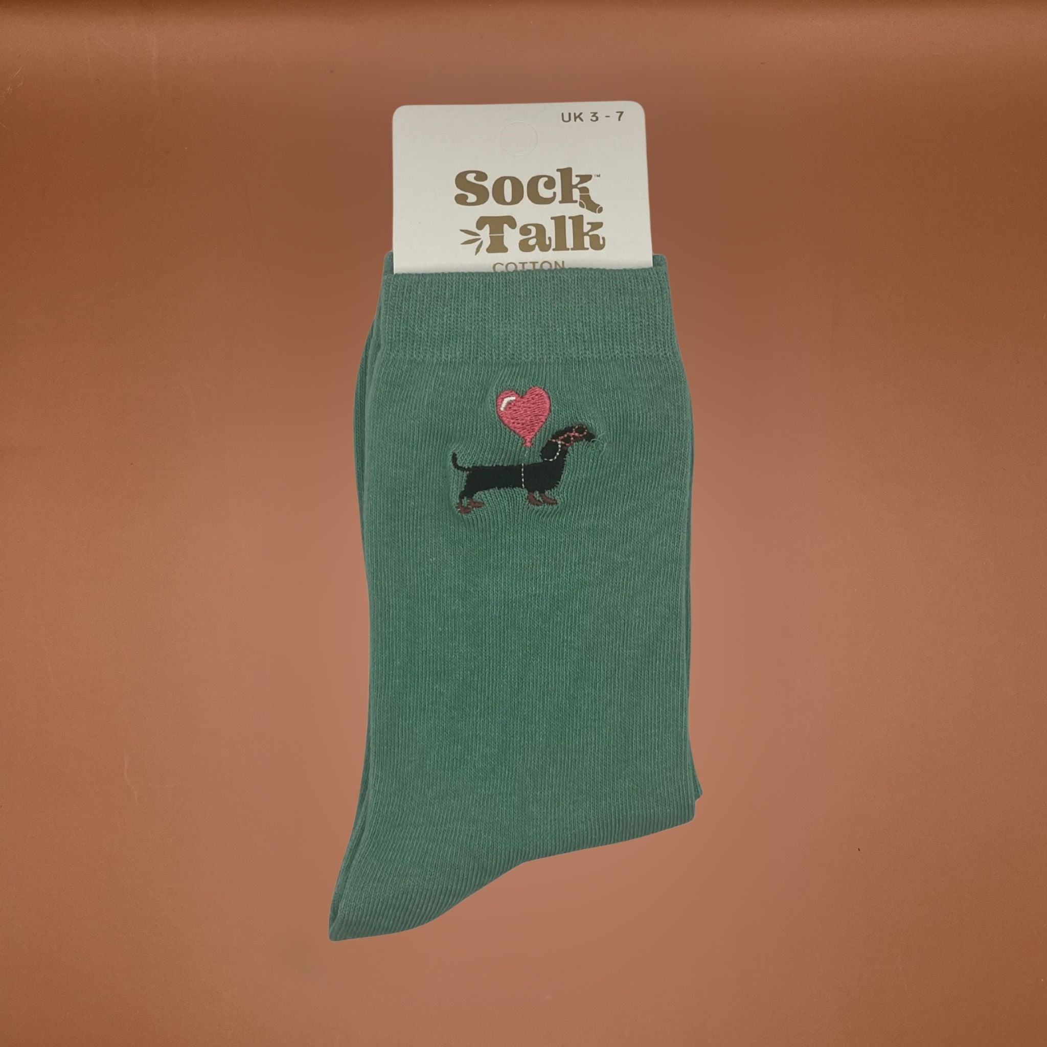 Green sock with dachshund and heart design on a brown background