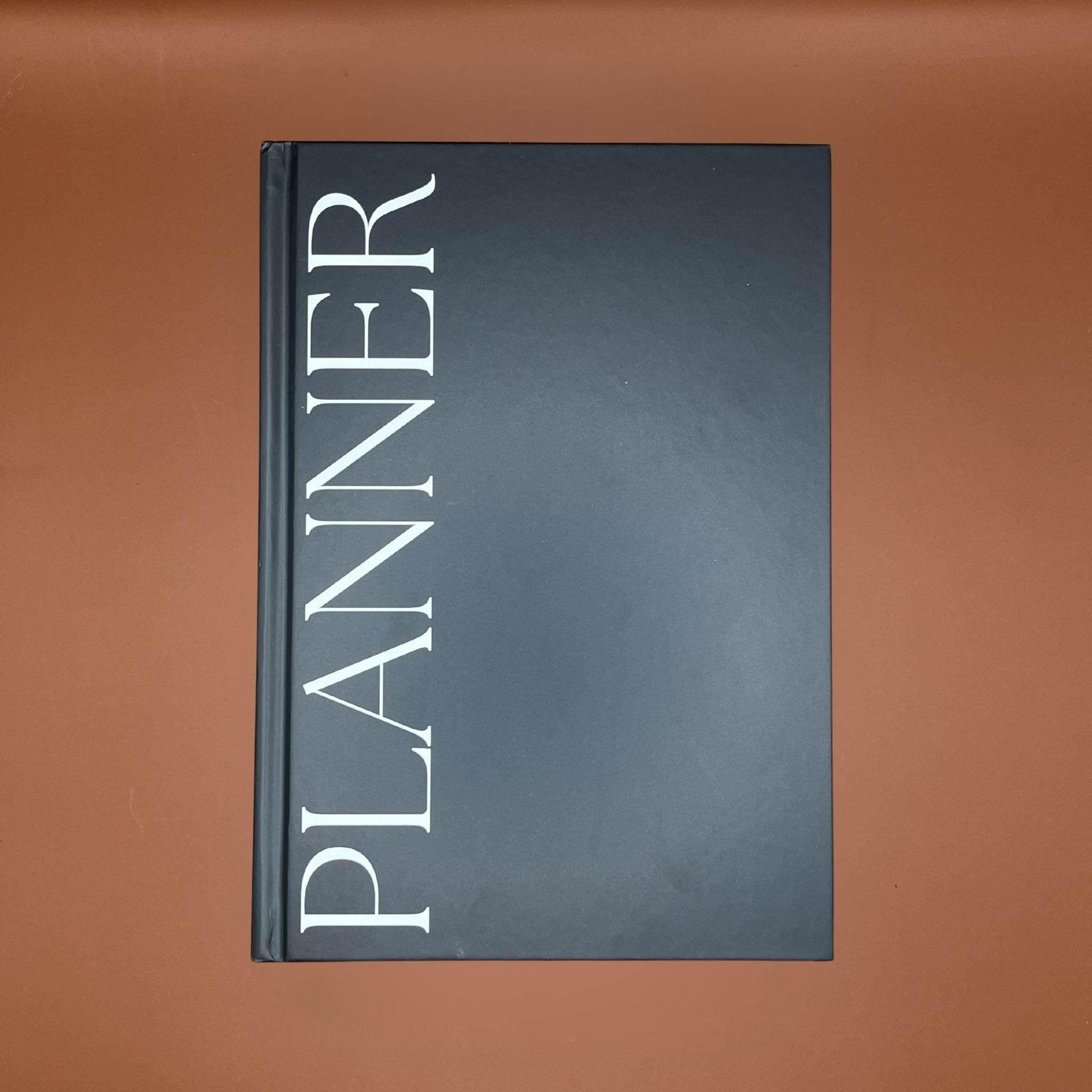 Black productivity planner book with 'PLANNER' text on front in white