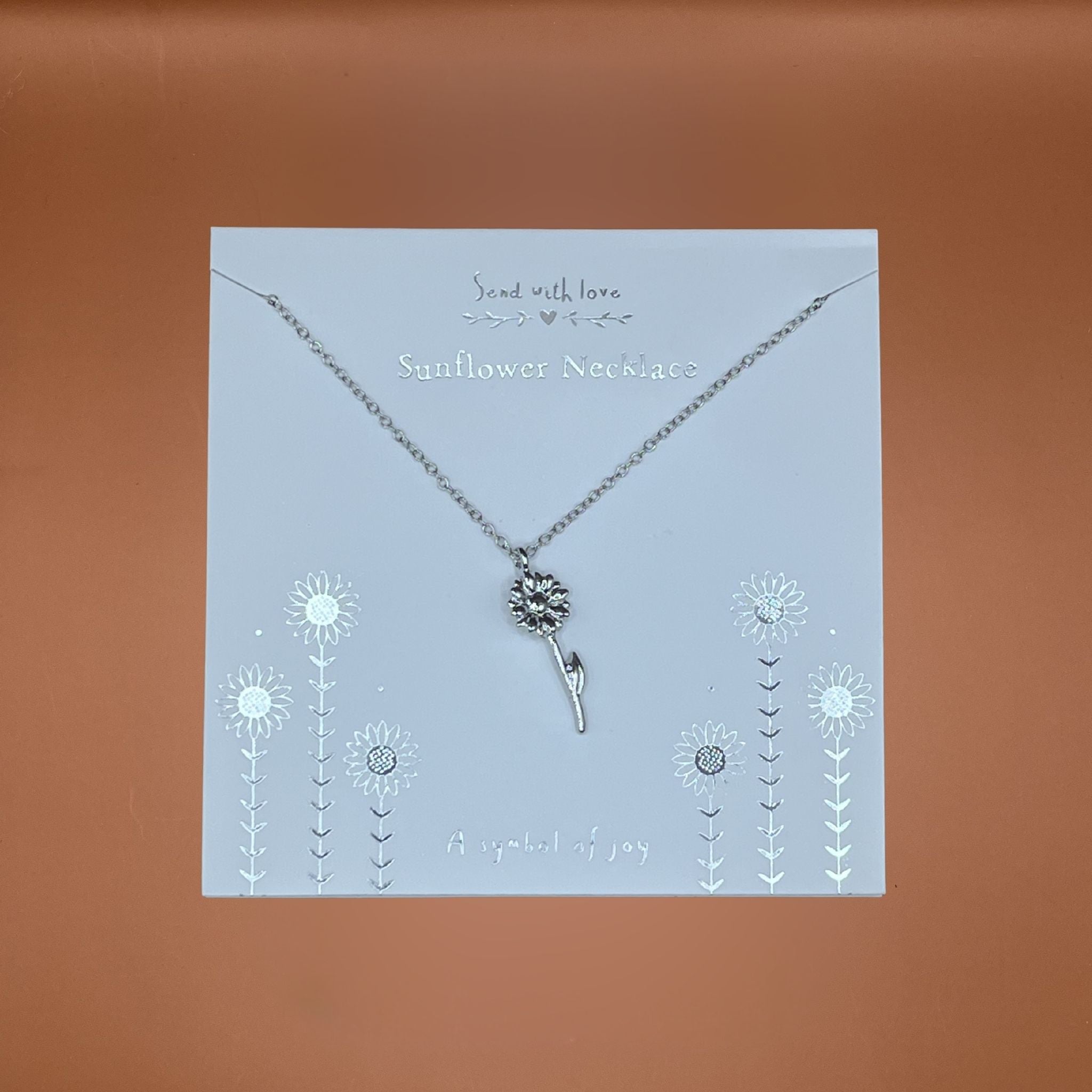 Silver sunflower necklace on a decorative card with floral designs