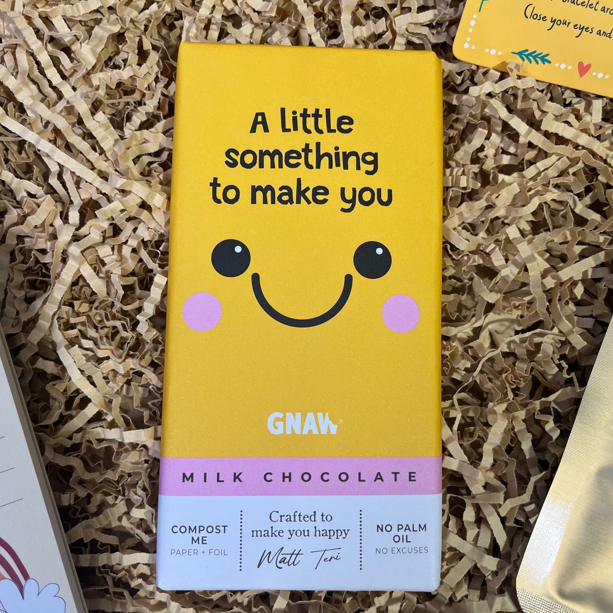 Gnaw milk chocolate bar with yellow packaging featuring a smiling face and the phrase “A little something to make you smile.”