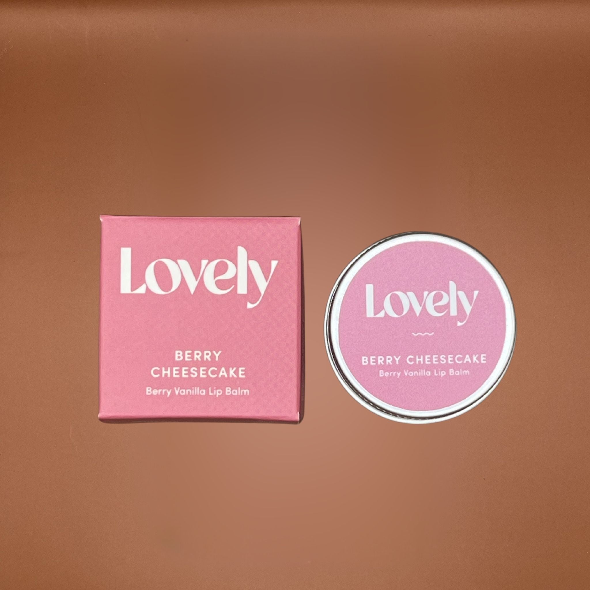 Pink 'Lovely' berry cheesecake lip balm packaging on a brown background