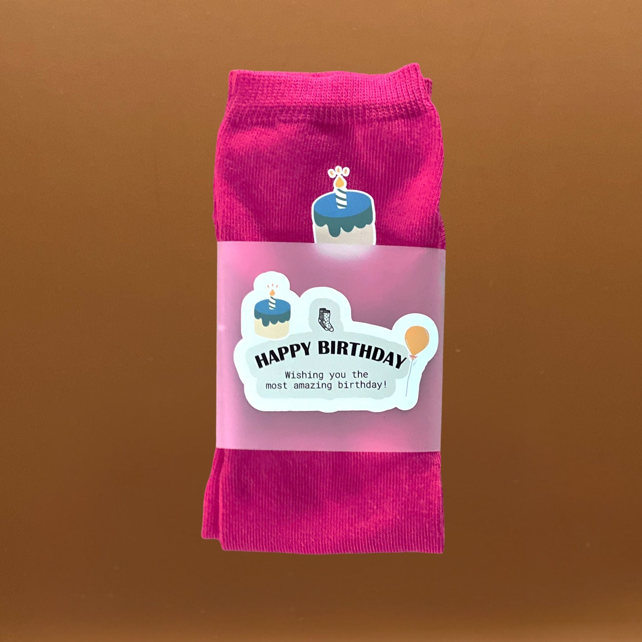Pink socks with a birthday cake design and a birthday themed label saying Happy Birthday.