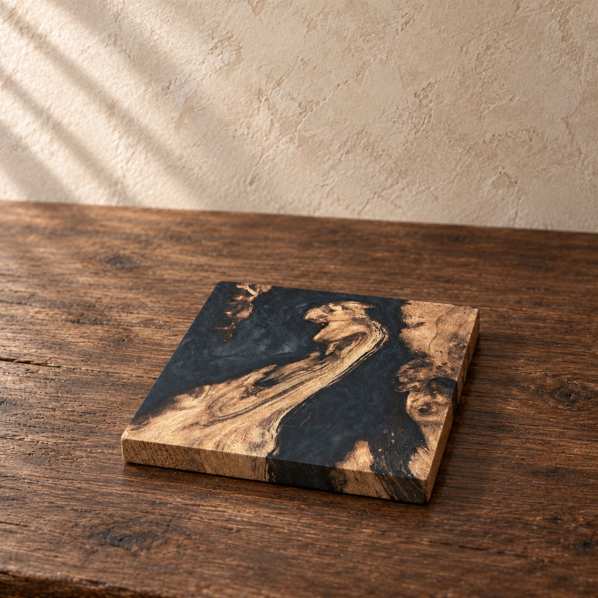 A square oak coaster with a marbled black and brown resin design, resting on a rustic dark wood table against a textured beige wall.