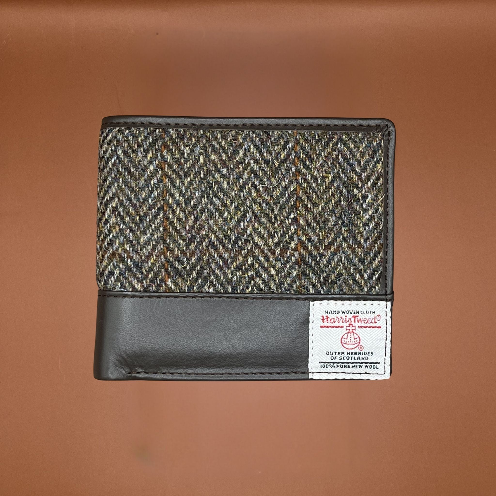 Wallet made from green and brown Harris Tweed fabric with brown leather trim and a Harris Tweed label on the front.