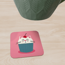 Pink birthday gift coaster, featuring a cute cat cupcake illustration topped with a cherry, placed on a wooden table.