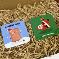 Two festive coasters, one featuring a cheerful toast character holding a drink in the snow, and another showing Santa balancing on one hand with a gift.