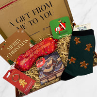 Festive Christmas gift box including men's gingerbread socks, a red sleep mask, chocolate bar, Santa coaster, gingerbread keyring, and Merry Christmas card.