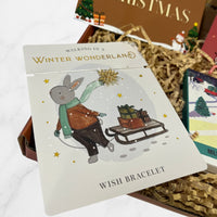 Winter-themed wish bracelet featuring a gold snowflake charm on a card with a festive bunny pulling a sleigh of presents.