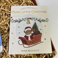 Christmas-themed wish bracelet featuring a gold tree charm on a card with a bear in a sleigh and festive decorations.