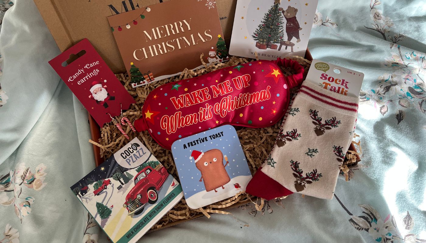 Festive Christmas letterbox gift box featuring cosy socks, a red “Wake Me Up When It’s Christmas” eye mask, candy cane earrings, chocolate, coaster, wish bracelet, and Merry Christmas card.