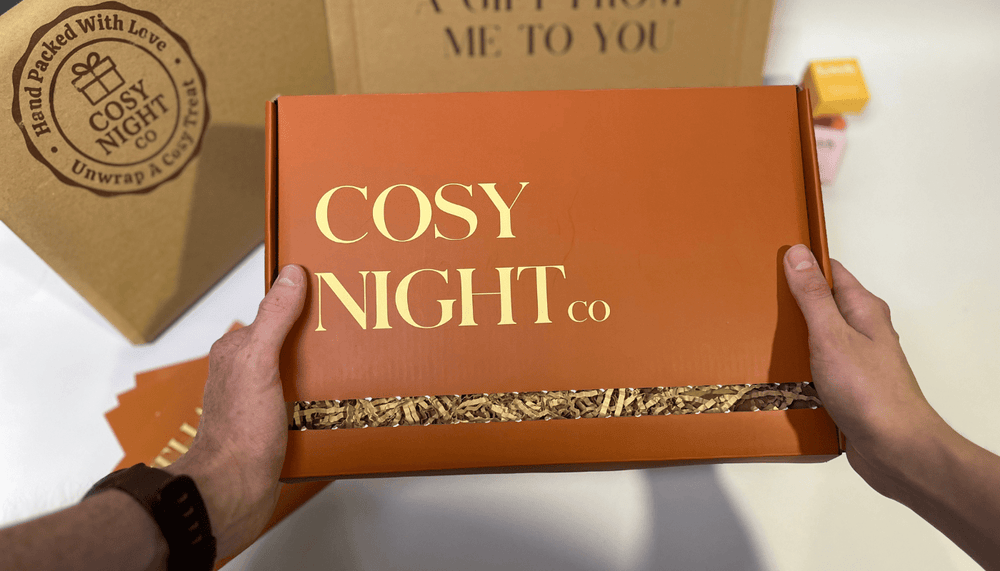 Hands holding a Cosy Night Co letterbox gift box with shredded paper packaging, perfect for gifting.