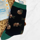Pair of black socks with green cuffs, heels, and toes featuring a cute repeating sloth pattern holding branches.