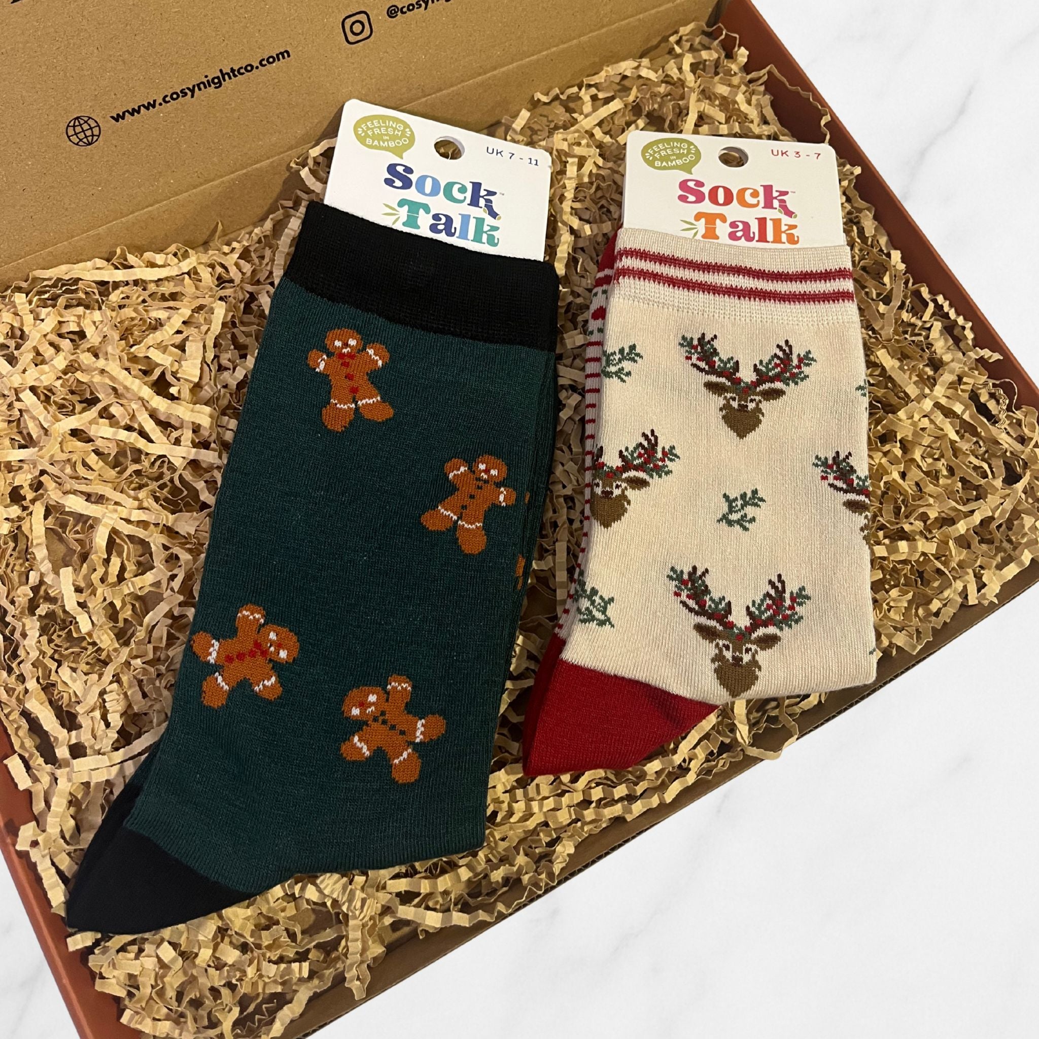 Two pairs of festive bamboo socks in a gift box. One with gingerbread men and one with reindeer and holly designs.
