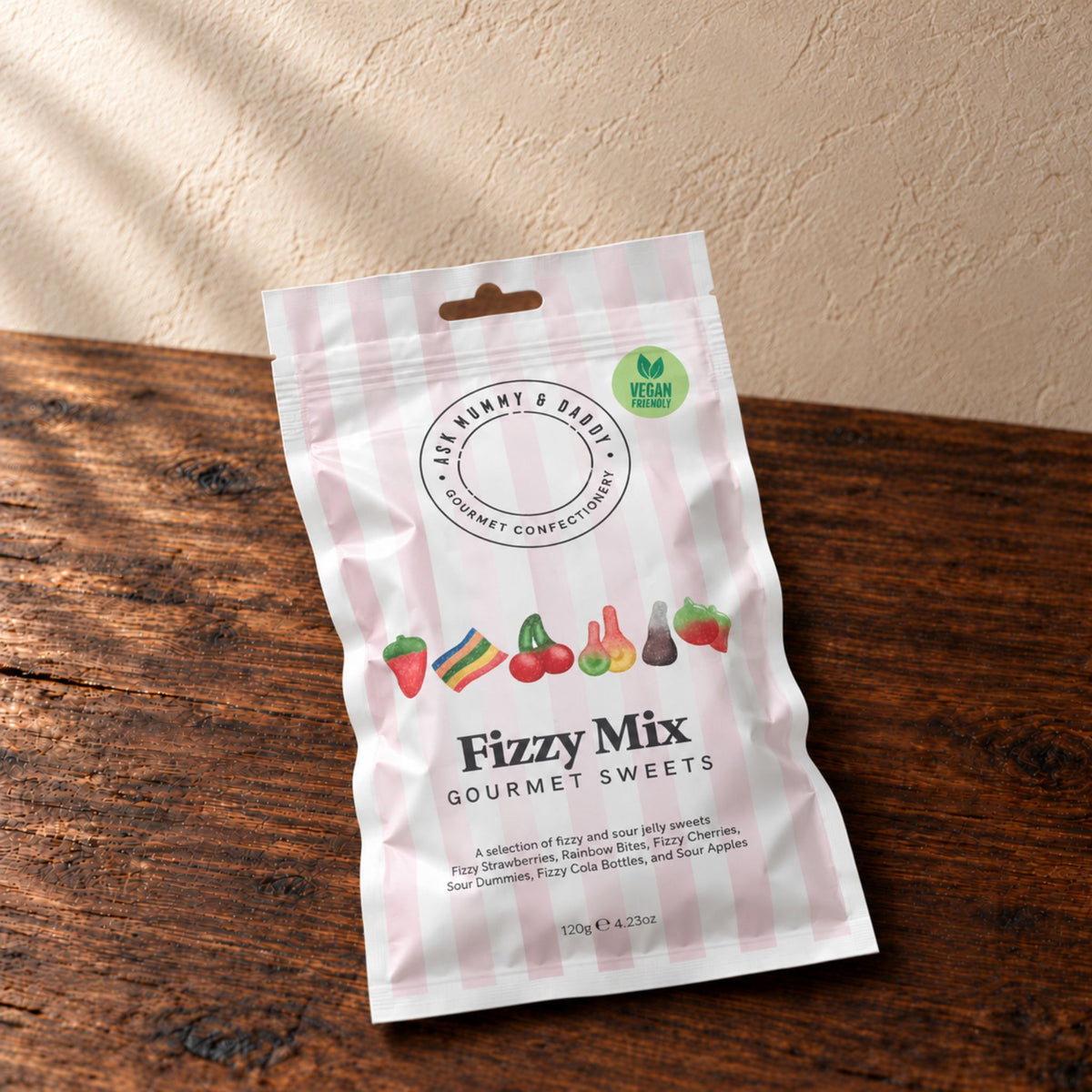a packet of fizzy mix gourmet sweets in striped packaging placed on a dark oak surface in front of a beige textured wall