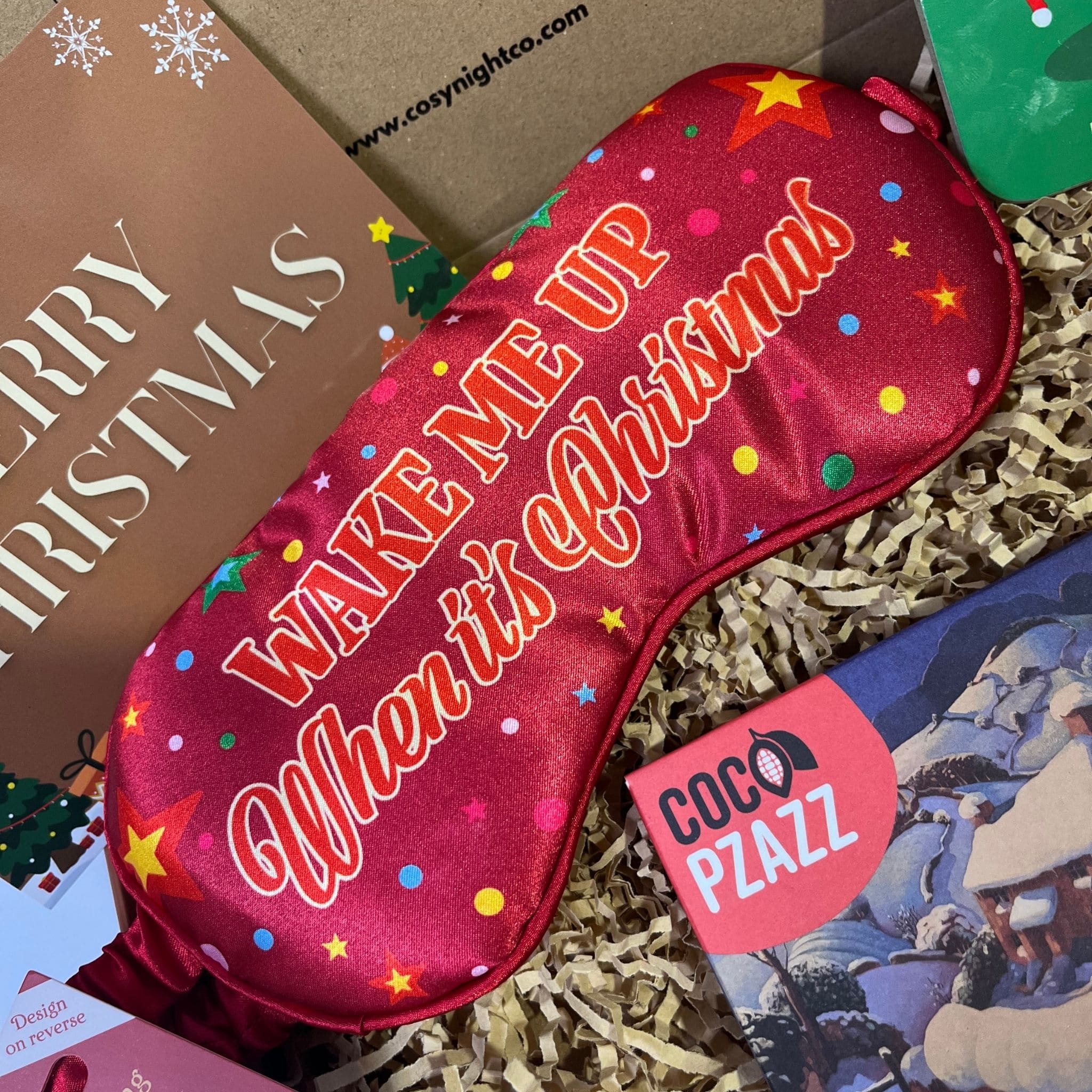 Festive red sleep mask with colourful dots and stars, featuring the phrase “Wake me up when it’s Christmas” in bold lettering.