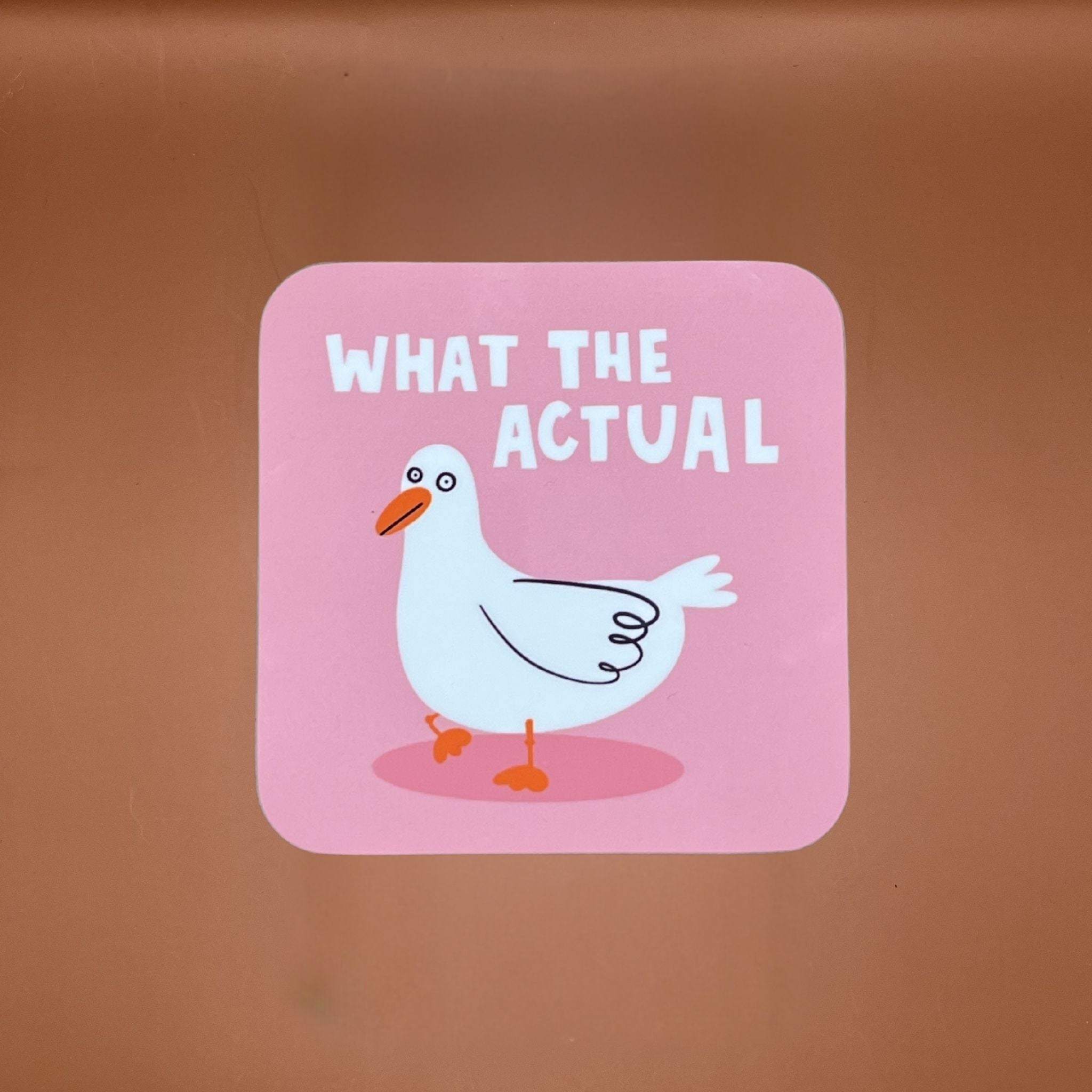 Coaster with a cartoon duck and text 'WHAT THE ACTUAL' on a pink background.