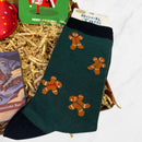 Dark green bamboo socks featuring a playful gingerbread man pattern, displayed in festive packaging with shredded paper filler.