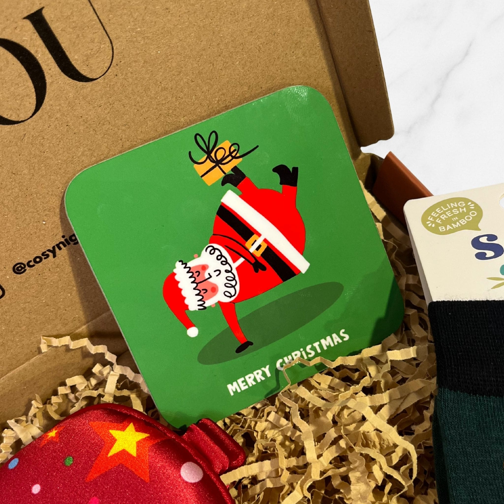 Green Christmas coaster featuring a playful illustration of Santa doing a handstand while holding a wrapped Christmas present.
