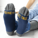 Blue socks with yellow text saying you make my toes tingle, worn by a person sitting on a light-coloured floor.