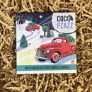 Coco Pzazz Milk Chocolate with Snow Flurries bar featuring a red vintage truck carrying a Christmas tree in a snowy winter scene.
