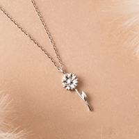 Silver sunflower necklace on a beige background.