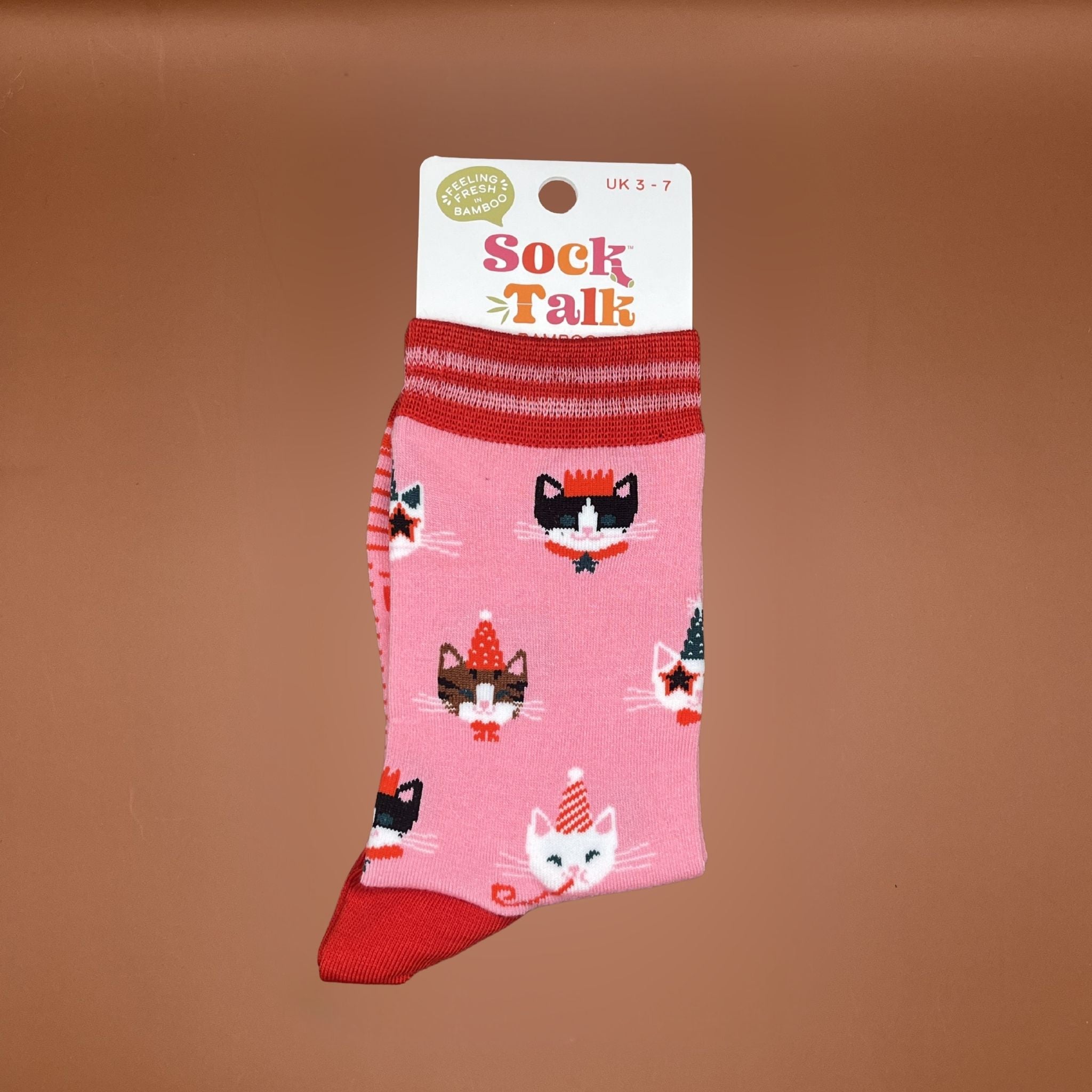 Pair of pink socks with red cuffs and toes, featuring repeating cat faces wearing party hats and crowns.