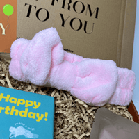 Soft pink fluffy headband with a bow design, displayed inside a gift box.