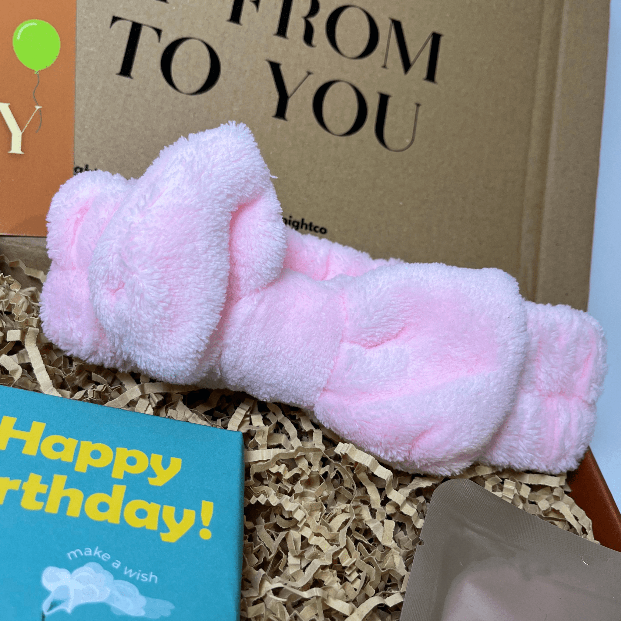 Soft pink fluffy headband with a bow design, displayed inside a gift box.