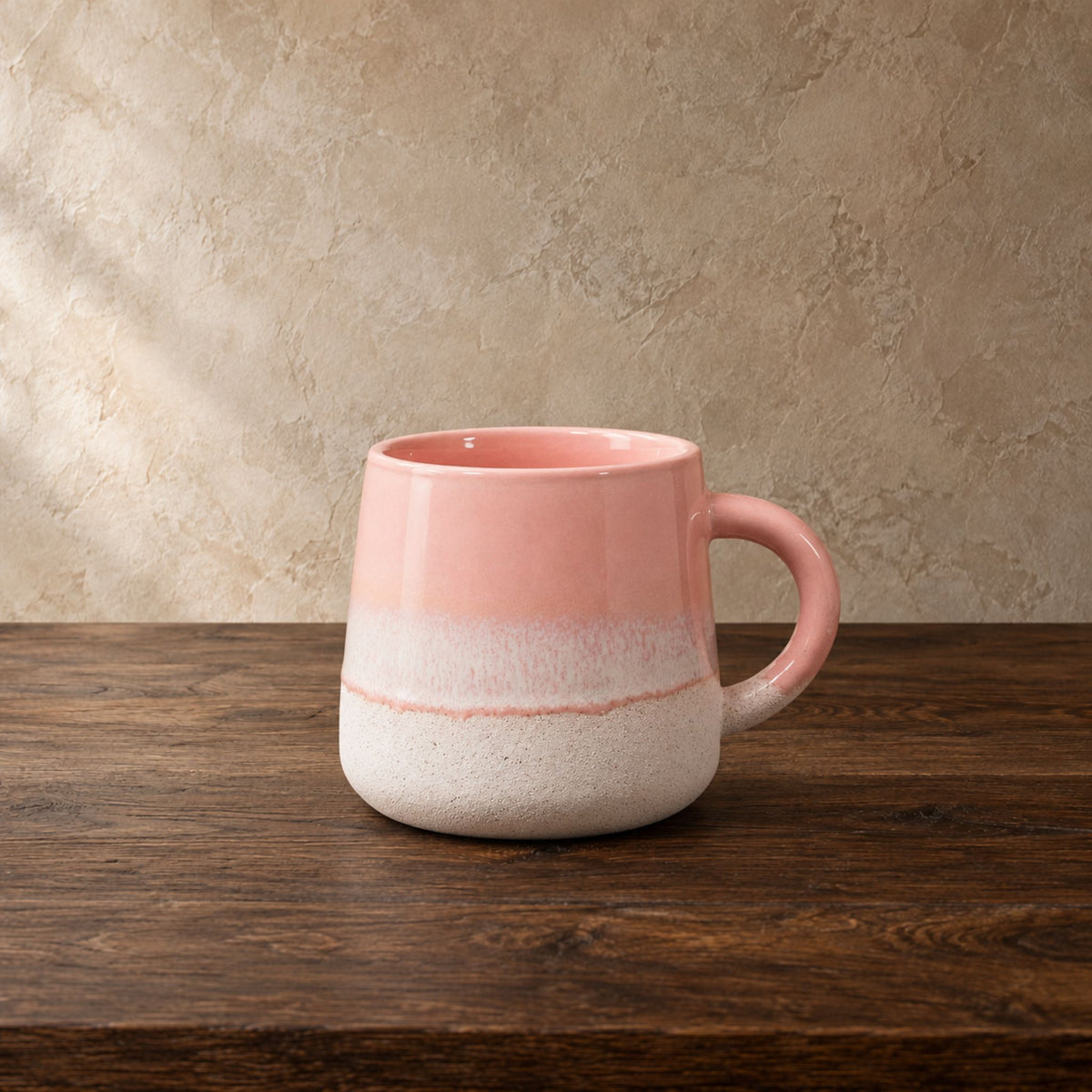 pink and white stoneware mug on a dark oak table in front of a beige textured wall.