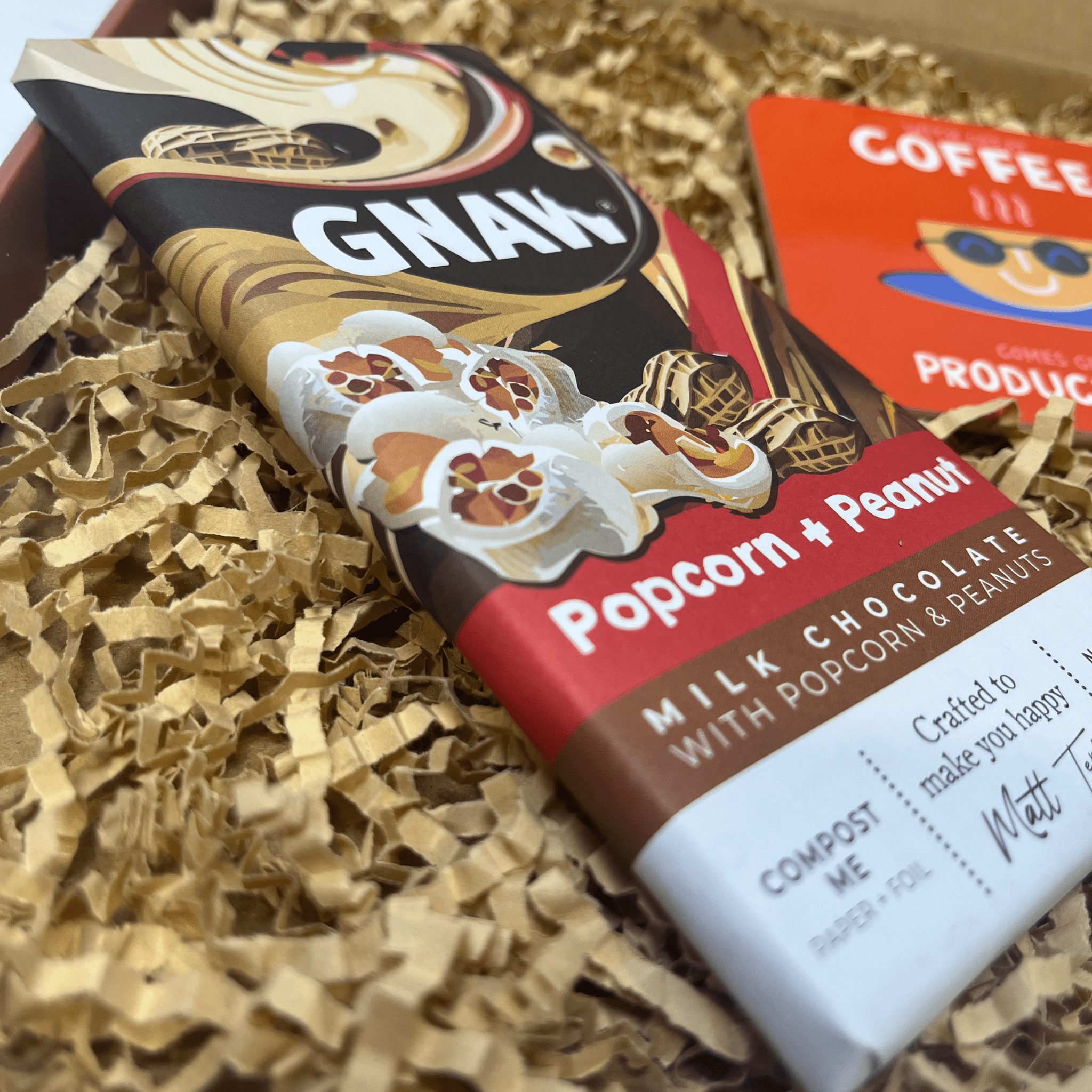 Close-up of Gnaw popcorn and peanut milk chocolate inside letterbox gift box.