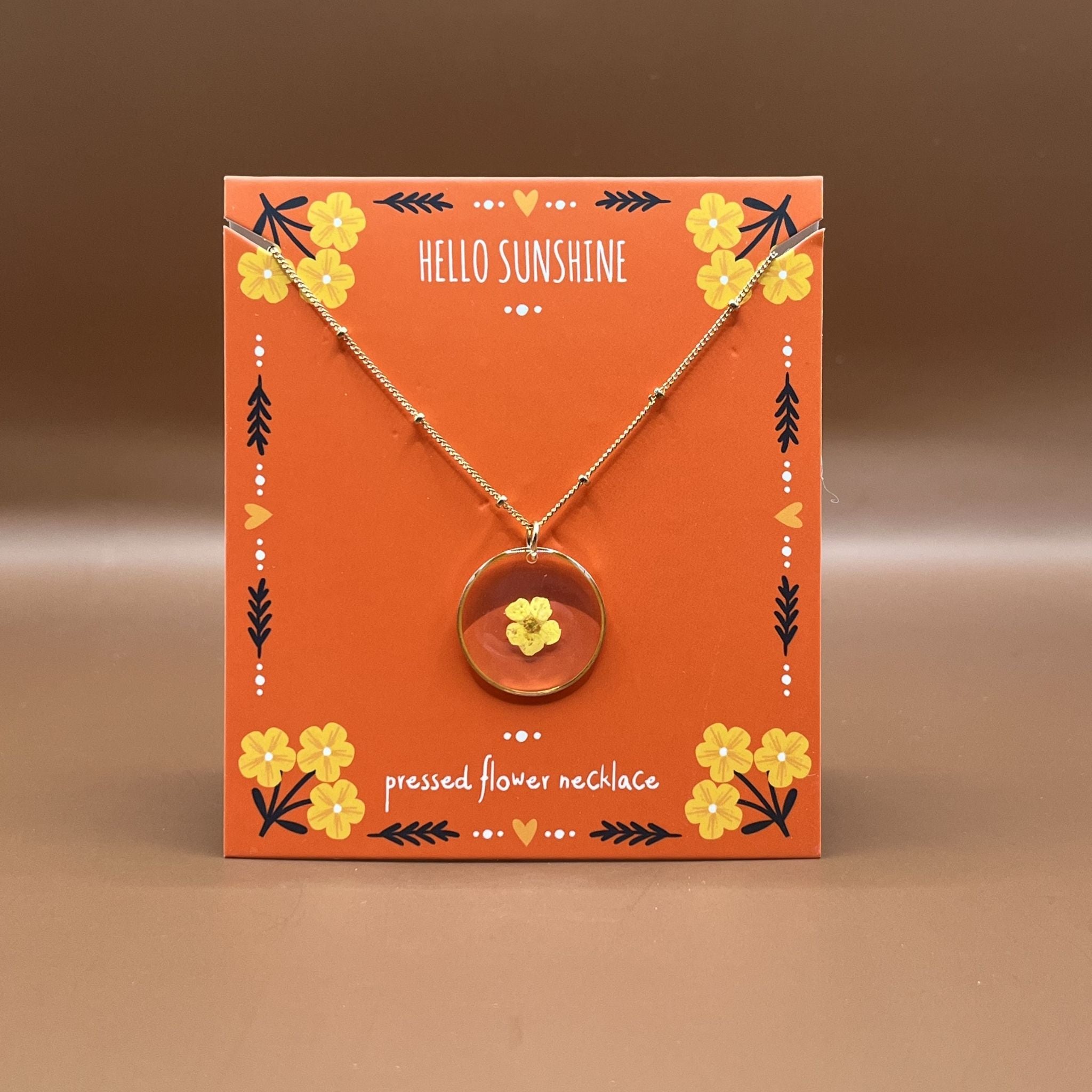 Necklace with a floral pendant on an orange card labeled 'Hello Sunshine'