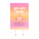 A rose quartz heart bracelet displayed on a pink and orange gradient card reading “you are loved.” The delicate pink string features gold beads, designed as a thoughtful reminder of love and positivity.