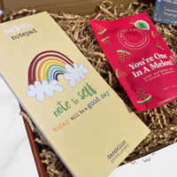 Positivity-themed “Note to Self” magnetic notepad and “You’re One In A Melon” watermelon gummies displayed inside a shredded paper gift box