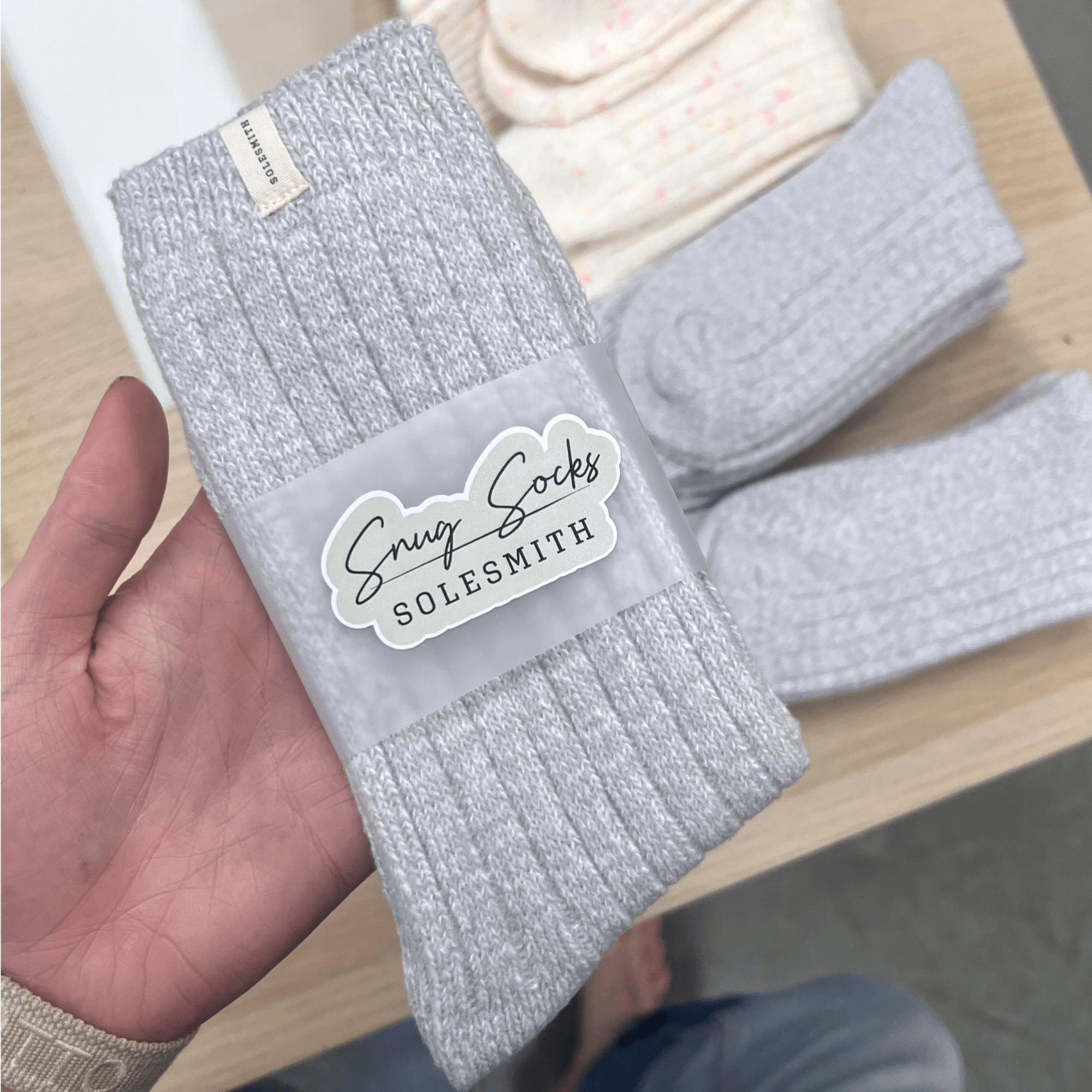 Grey sock with 'Snug Socks Solesmith' label held by a hand above a table