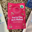 Bright pink packet of “You’re One In A Melon!” sour watermelon vegan gummies by Ask Mummy & Daddy, placed on shredded paper